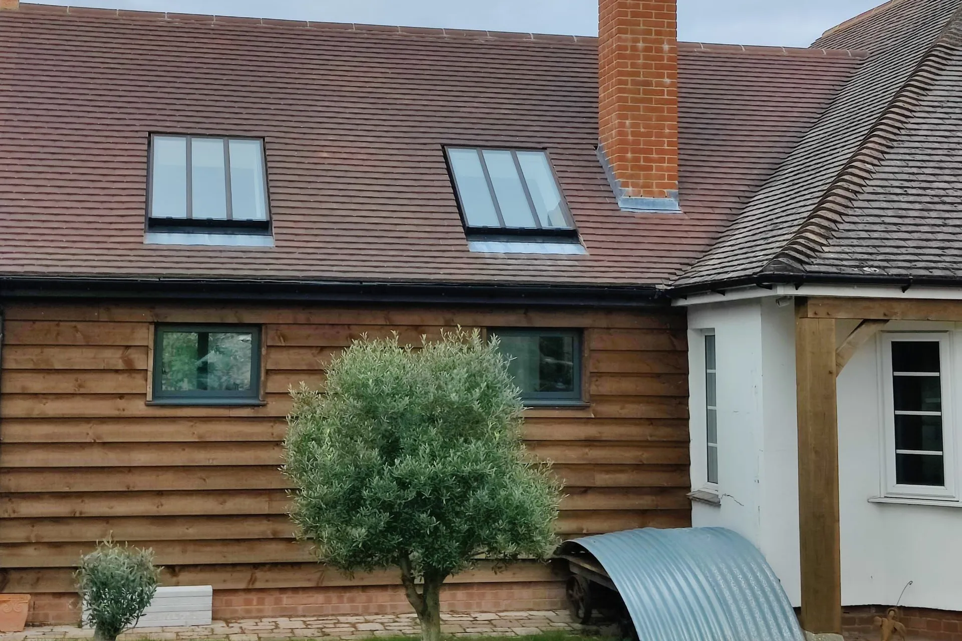 A timber-clad house with a clay tiled roof, brick chimney and roof windows